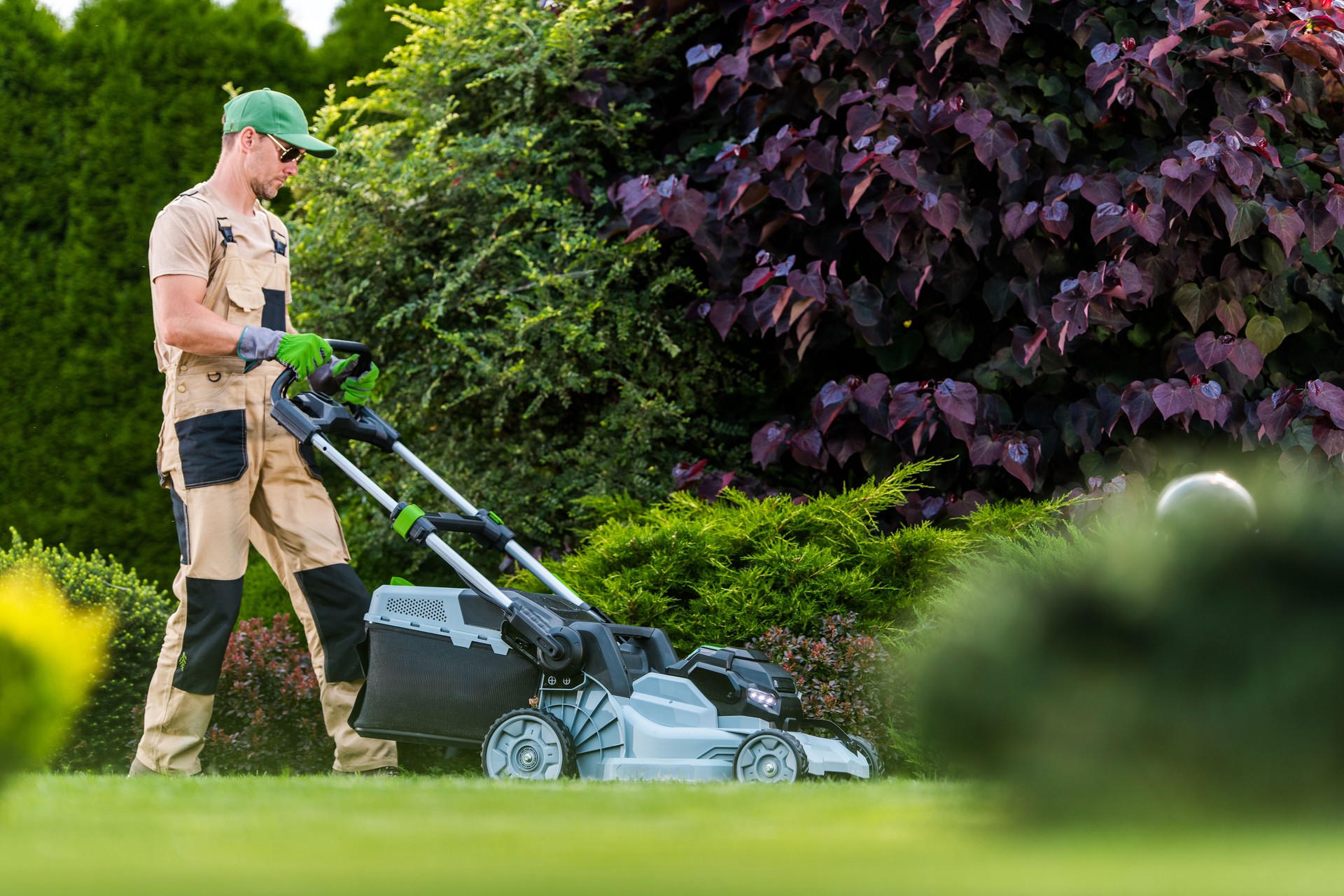 Gardener Using a Lawn Mower to Maintain a Vibrant Garden During a Sunny Afternoon